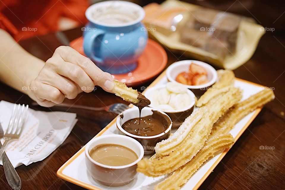 Churro. A hand holding a piece of Churro dipping in a dark chocolate sauce. Selective focus