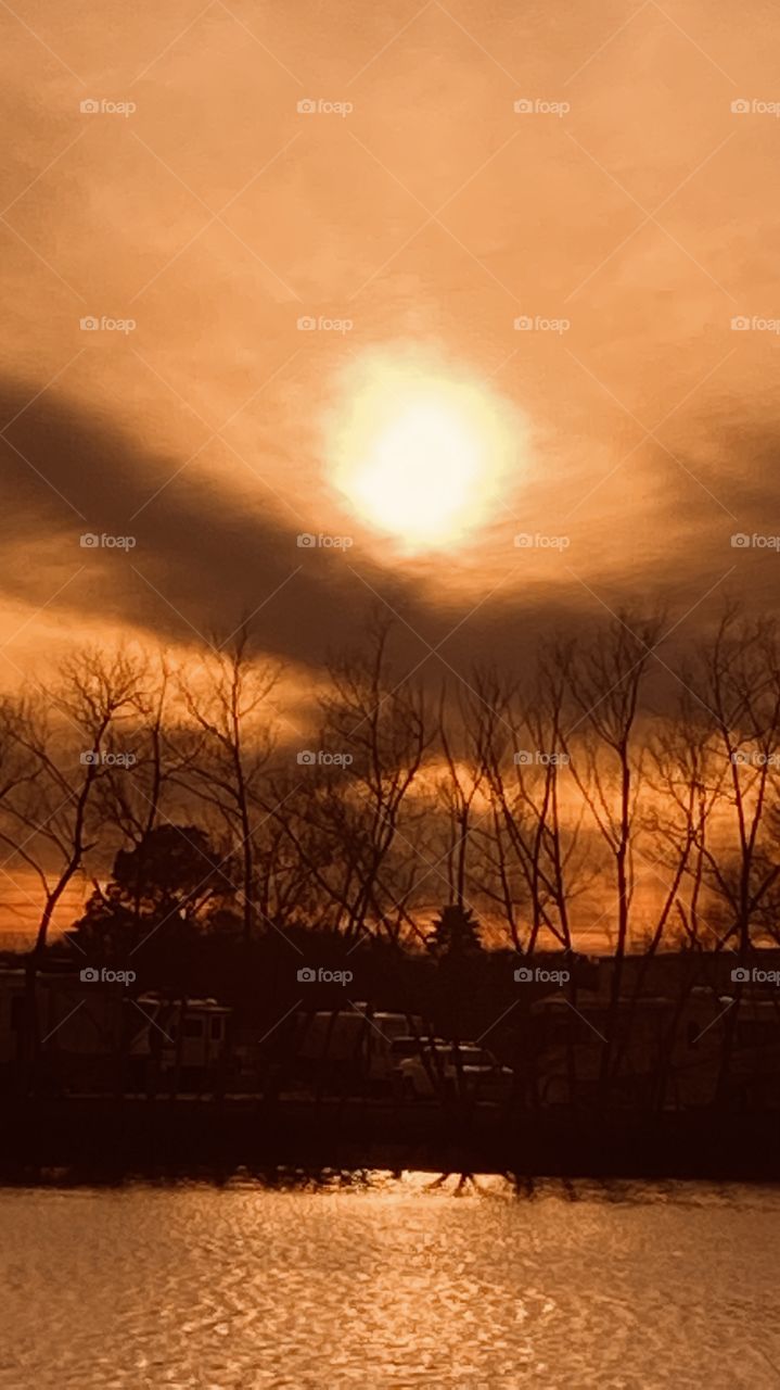 Alot going on with pic. Beautiful Defined Sun shaded by high clouds. More defined dark Clouds. Reflections of trees clouds sun seen on Lake Waters. 