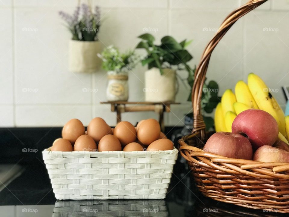 Using eco friendly reusable eggs basket and reusable bamboo basket with full of fresh fruits instead of using plastic containers and background covered with wooden stand and on that stand a reusable eco friendly plant containers.