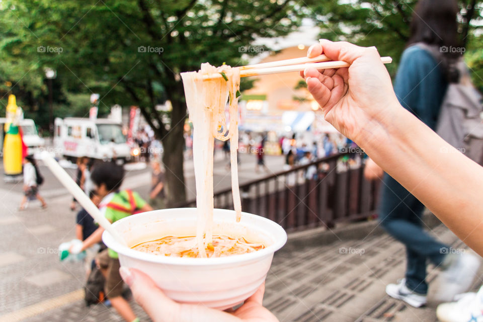 woman holding rice noodle by chopsticks at street.street market food