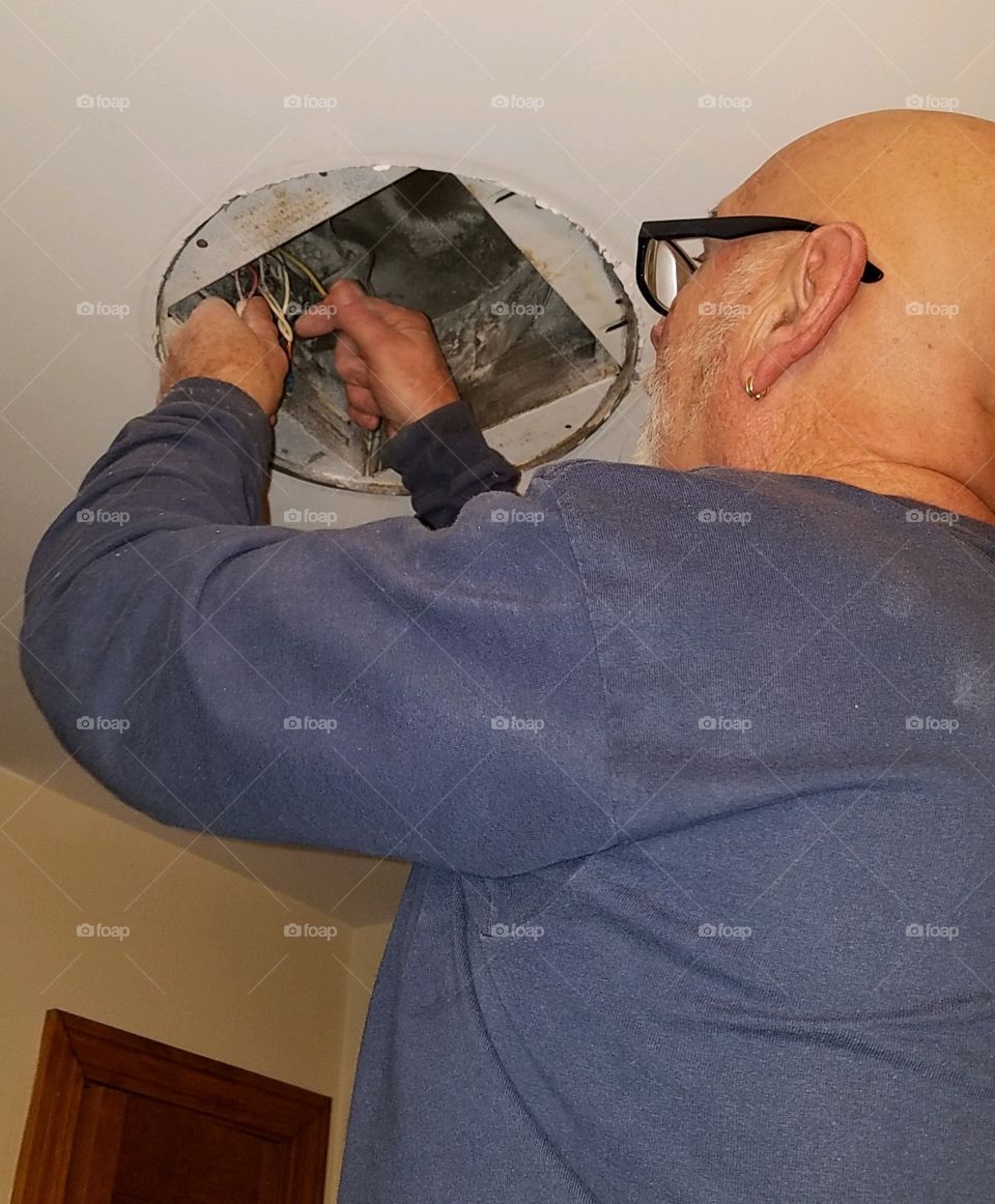 Man replacing ceiling light and fan in bathroom, updating old with the new and improved.