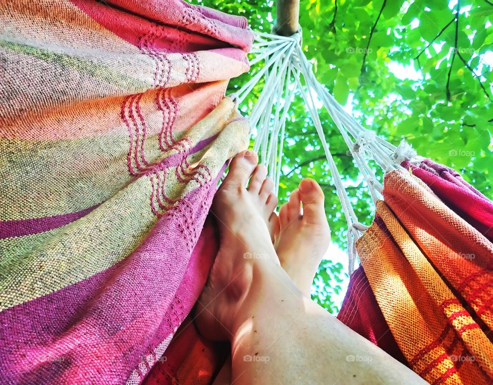 Feeds of a woman relaxing in a red and orange hammock with a high angle view to a green leaves canopy