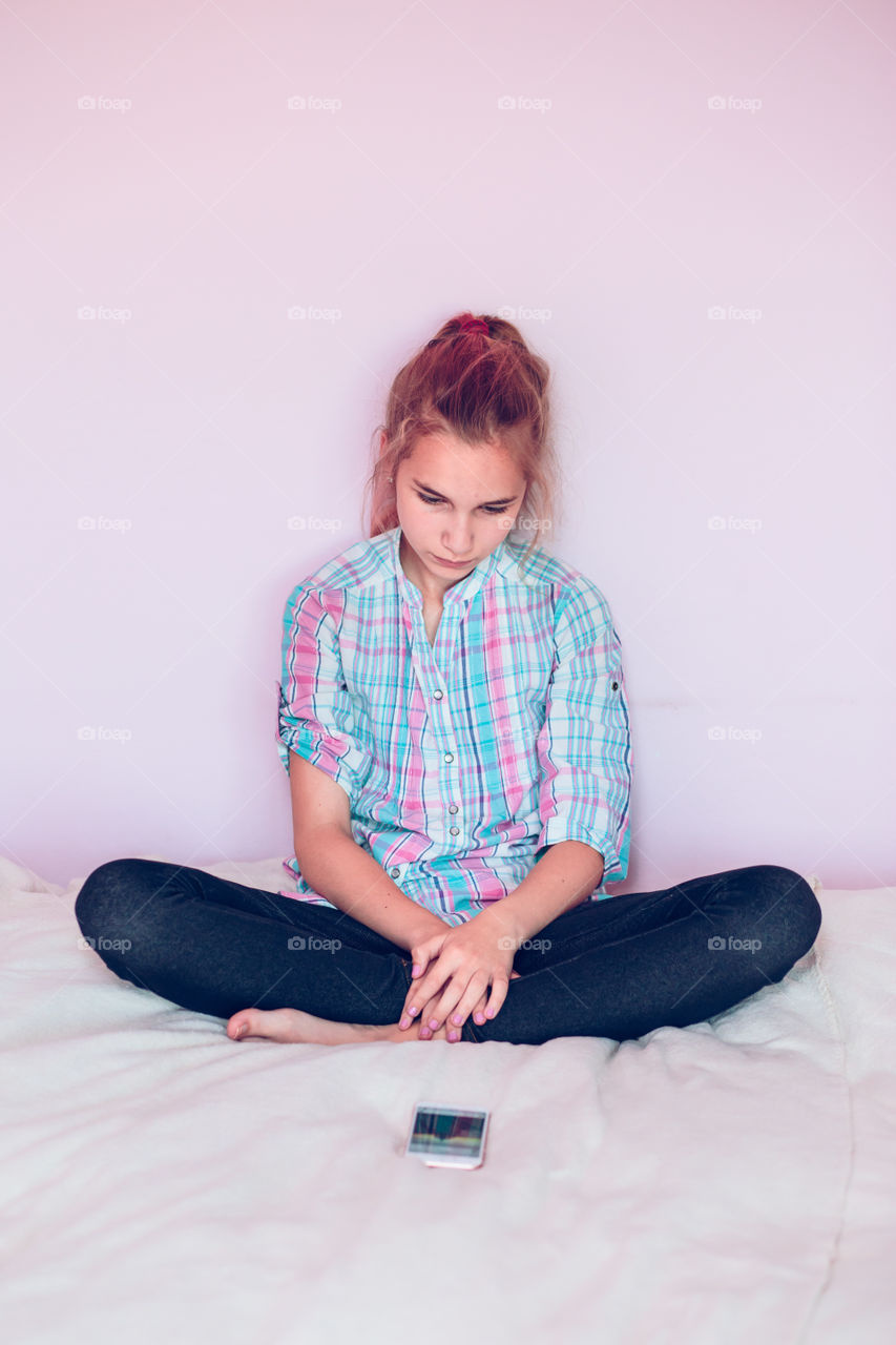 Young girl sitting on bed and looking at mobile phone