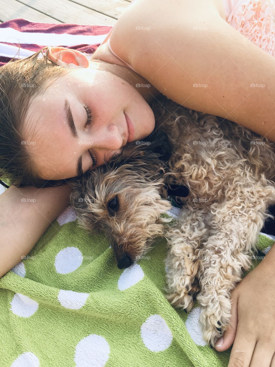 A young girl and her dog rest after playing at the lake on a warm summer day, cuddling on a beach towel