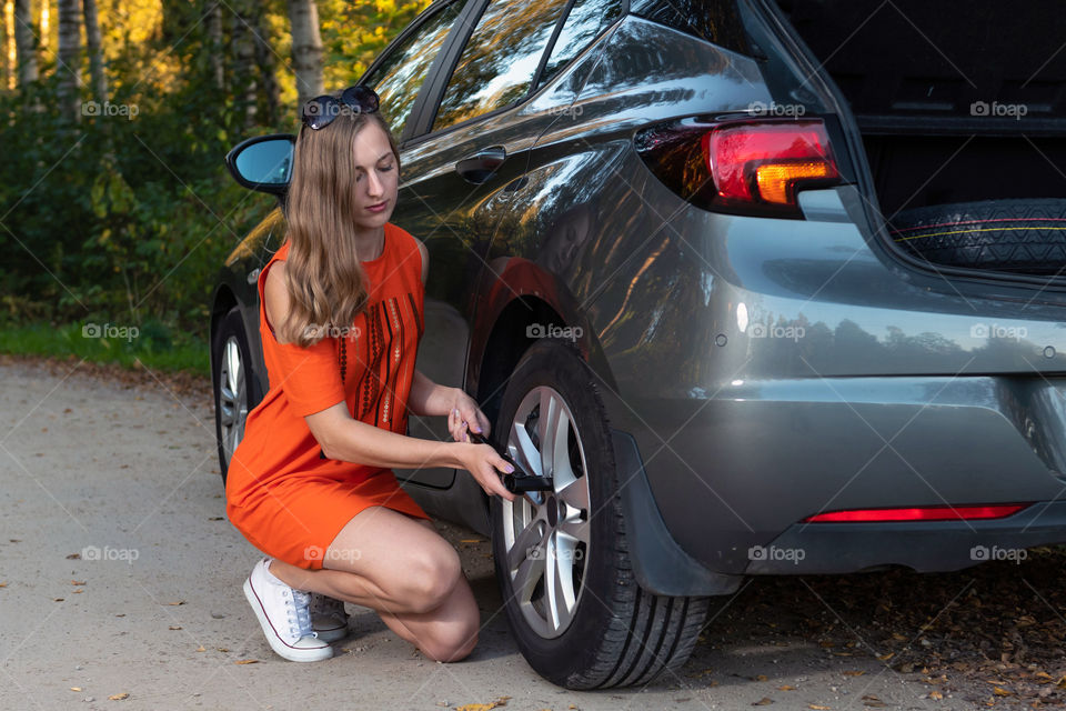 Beautiful, young woman changing dameged wheel and fixing it.