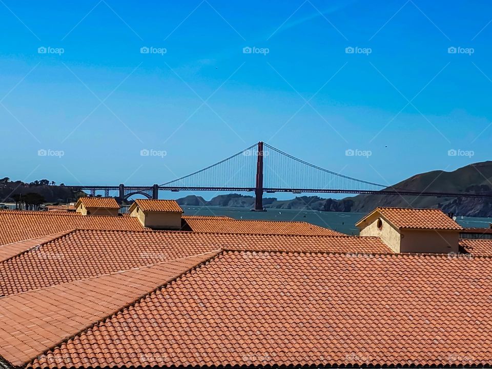 View of the Golden Gate Bridge from the hill overlooking Fort Mason in San Francisco California, beautiful red terracotta roofs in the foreground with calm surf on a stunning warm clear day
