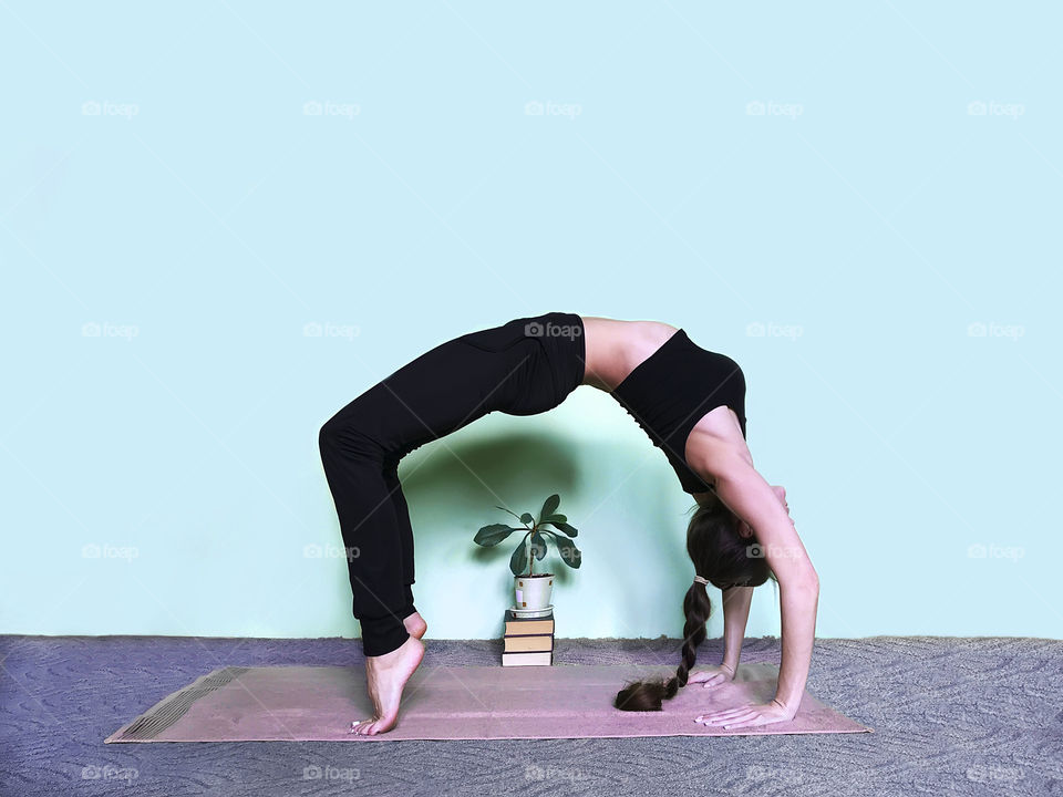 Young woman with long hair doing yoga next to the house plant in front of a blue monochrome wall 