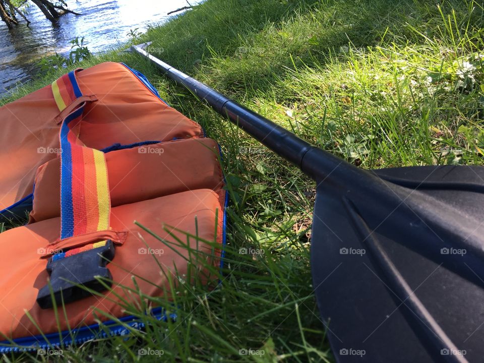 Orange life jacket on grassy shore next to lake and canoe and kayak paddle summertime safety and vacation travel background image 