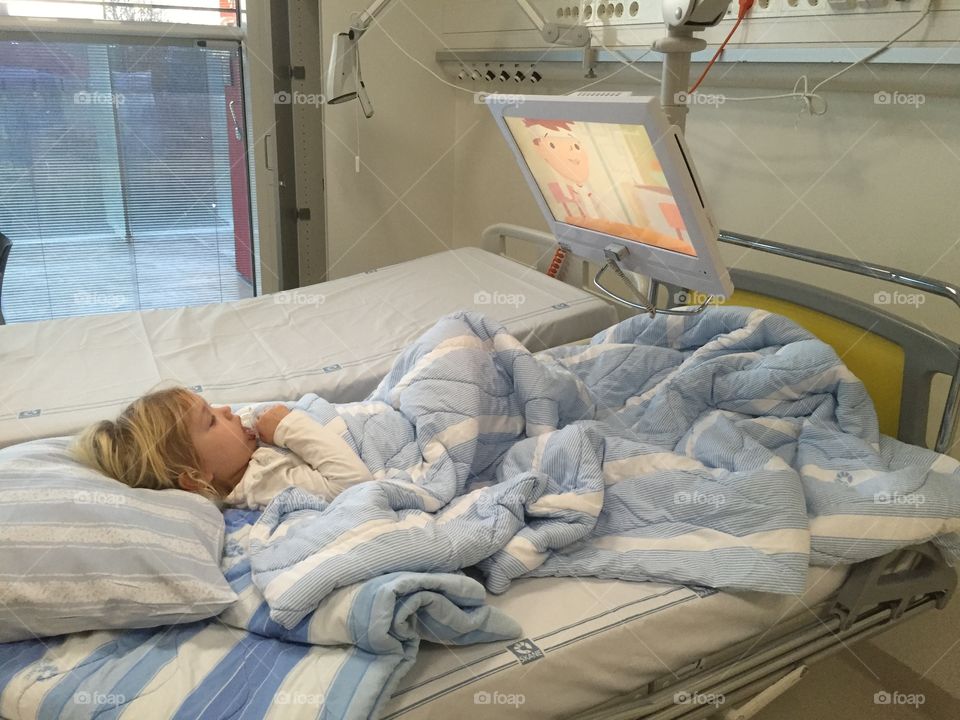 Little girl watching Tv at in the bed at hospital.