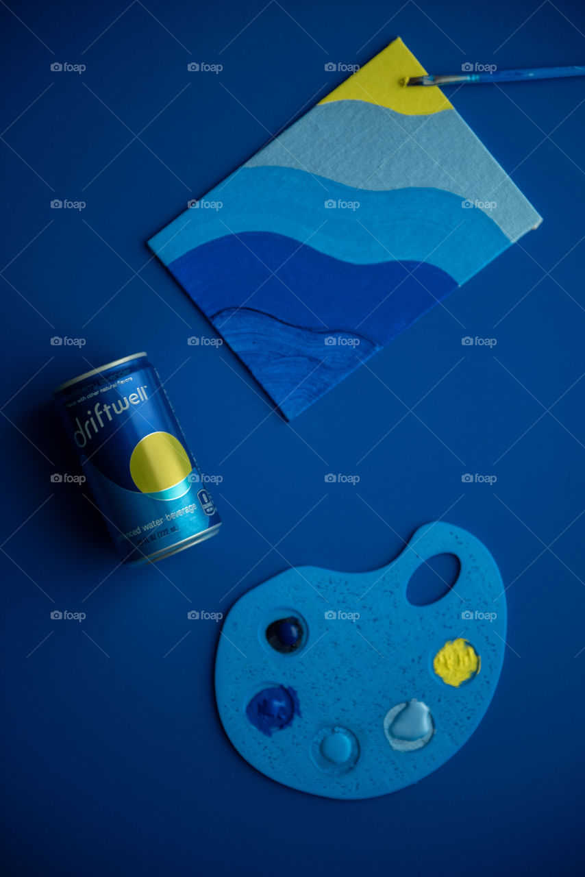 Monochromatic flat lay of a can of Driftwell on a blue background with a blue painting