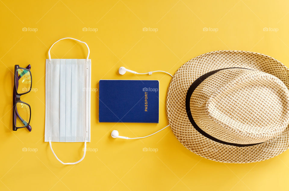 Travel after Covid-19 and new normal concepts. Top view of medical face mask, hand gel sanitizer, headphones and beach hat on yellow background close up. Creative ideas of prevent coronavirus.