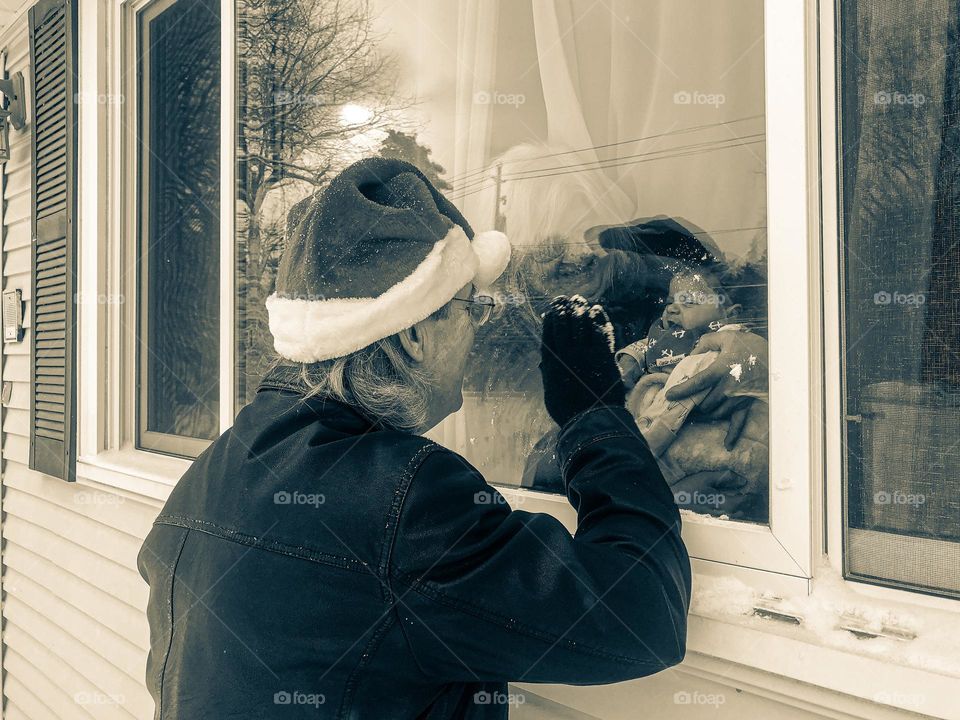 Grandpa surprises baby at the window, Grandpa dressed as Santa surprises baby girl through window, baby looking through a window, Santa peeks into a window in December, Santa surprises baby, looking at Santa through a window, monochrome portrait 