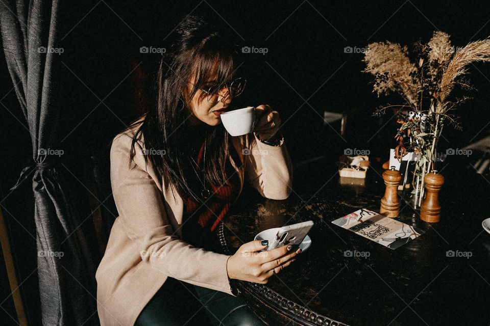 Beautiful brunette girl drinking coffee in street cafe and look at mobile phone