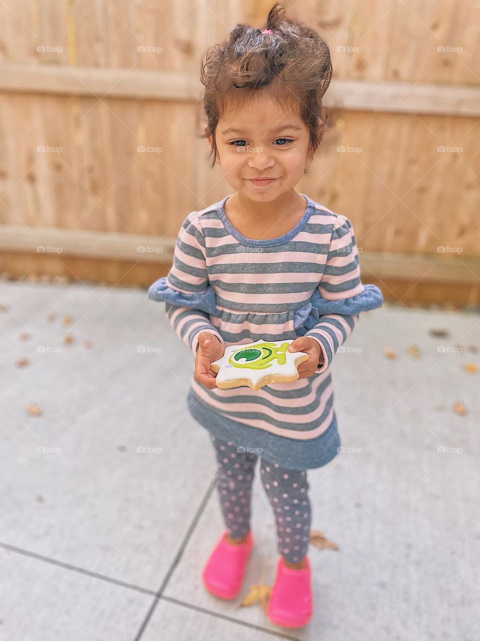 Toddler girl holding sugar cookie, monsters Inc. sugar cookie, very decorative sugar cookie, pictures with icing, cute little girl with cookie, eating cookies outside 