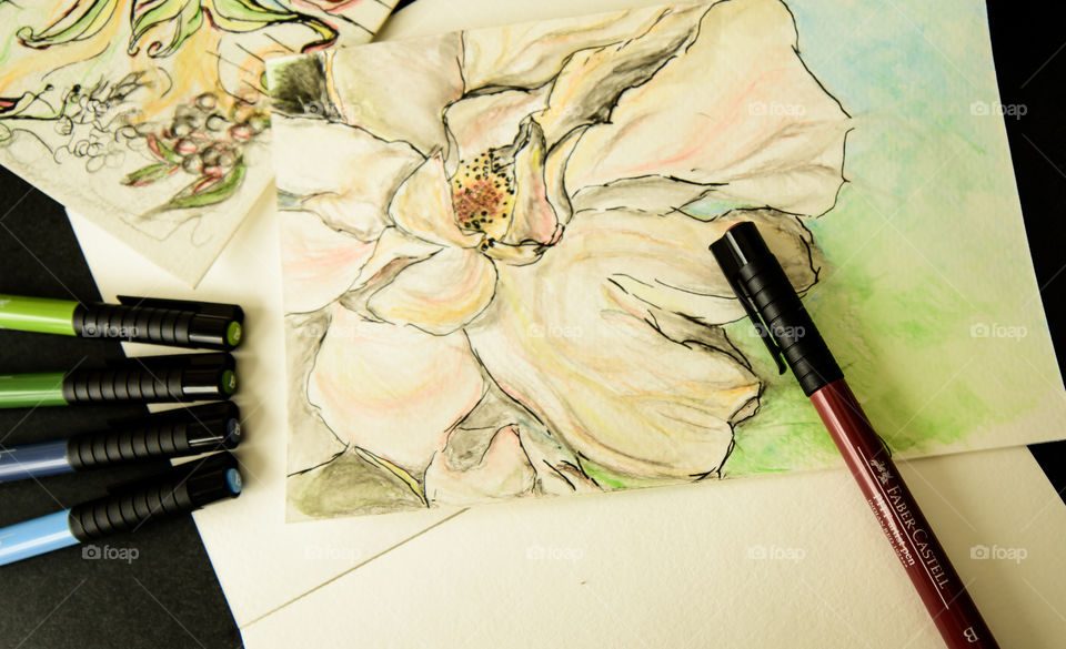 Faber-Castell PITT artist pens on desk with watercolor style painting sketch using Faber-Castell pens high angle view of spring flowers on sketch books 