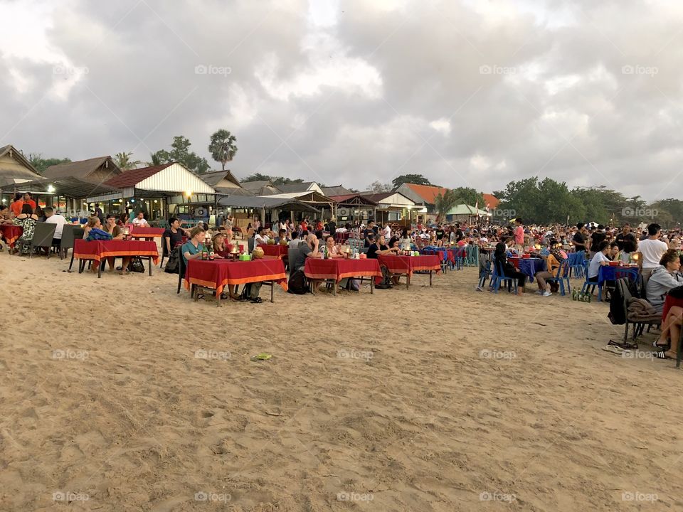 Dinner during sunset beach crowd. Tables and chairs, red tablecloths. Seafood extravaganza. Bali, Indonesia. 2018.