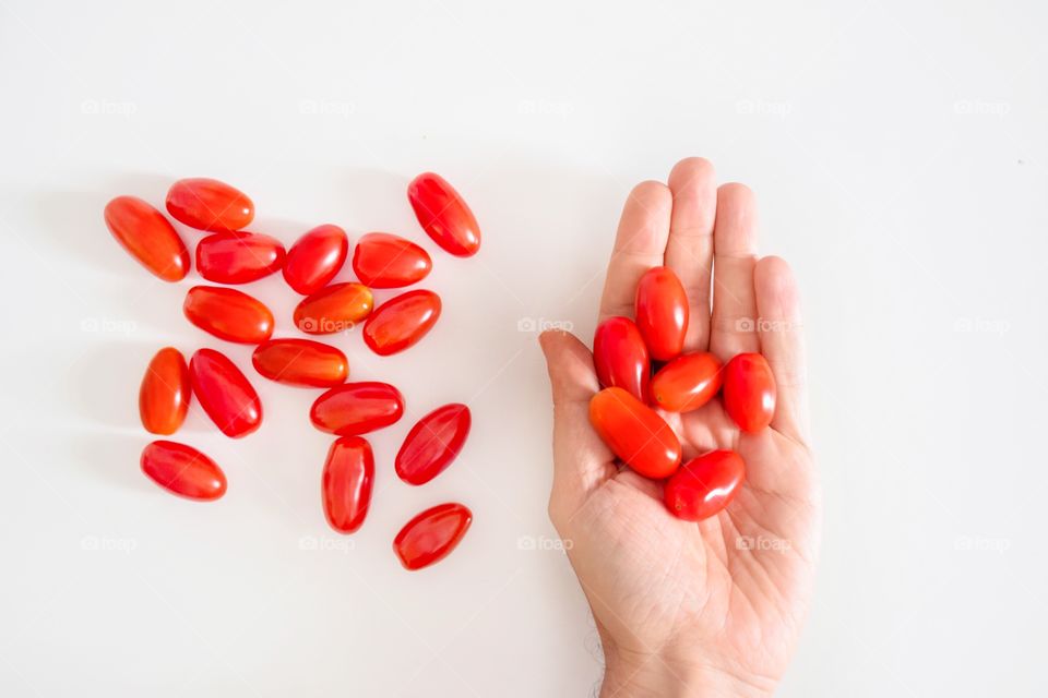Flat lay of a hand holding cherry tomatoes on a white background