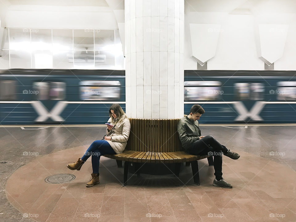 Young man and woman using mobile phones in front of a moving subway train 