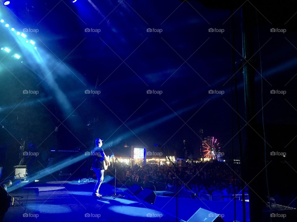 Singing to the crowds. Lighting. Stage lights. People. Outdoor stage. People. Blue lights. Musician. 