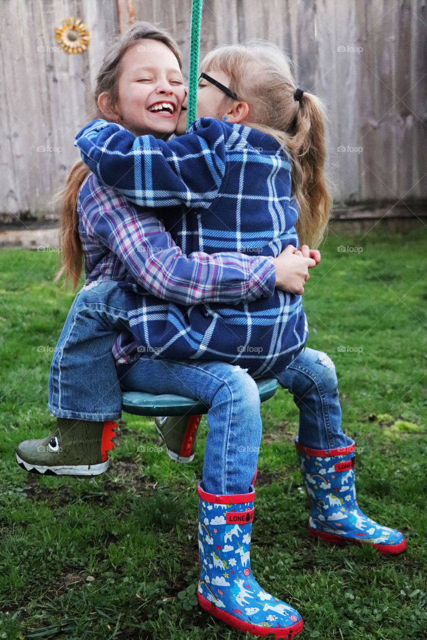 Two sisters hugging each other on the swing