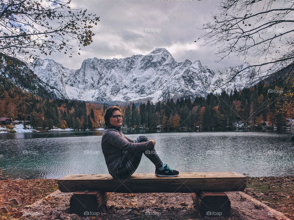 A woman traveler sitting and admires the view of the snow-capped mountain peaks above italian lake.