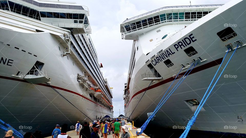 Two large cruise ships are seen at a port of call in the Bahamas. A crowd of unrecognizable people.