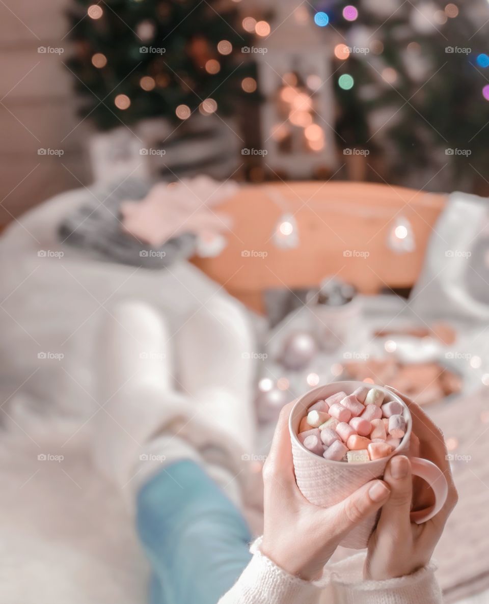 Cup with marshmallows in female hands on a background of Christmas decor