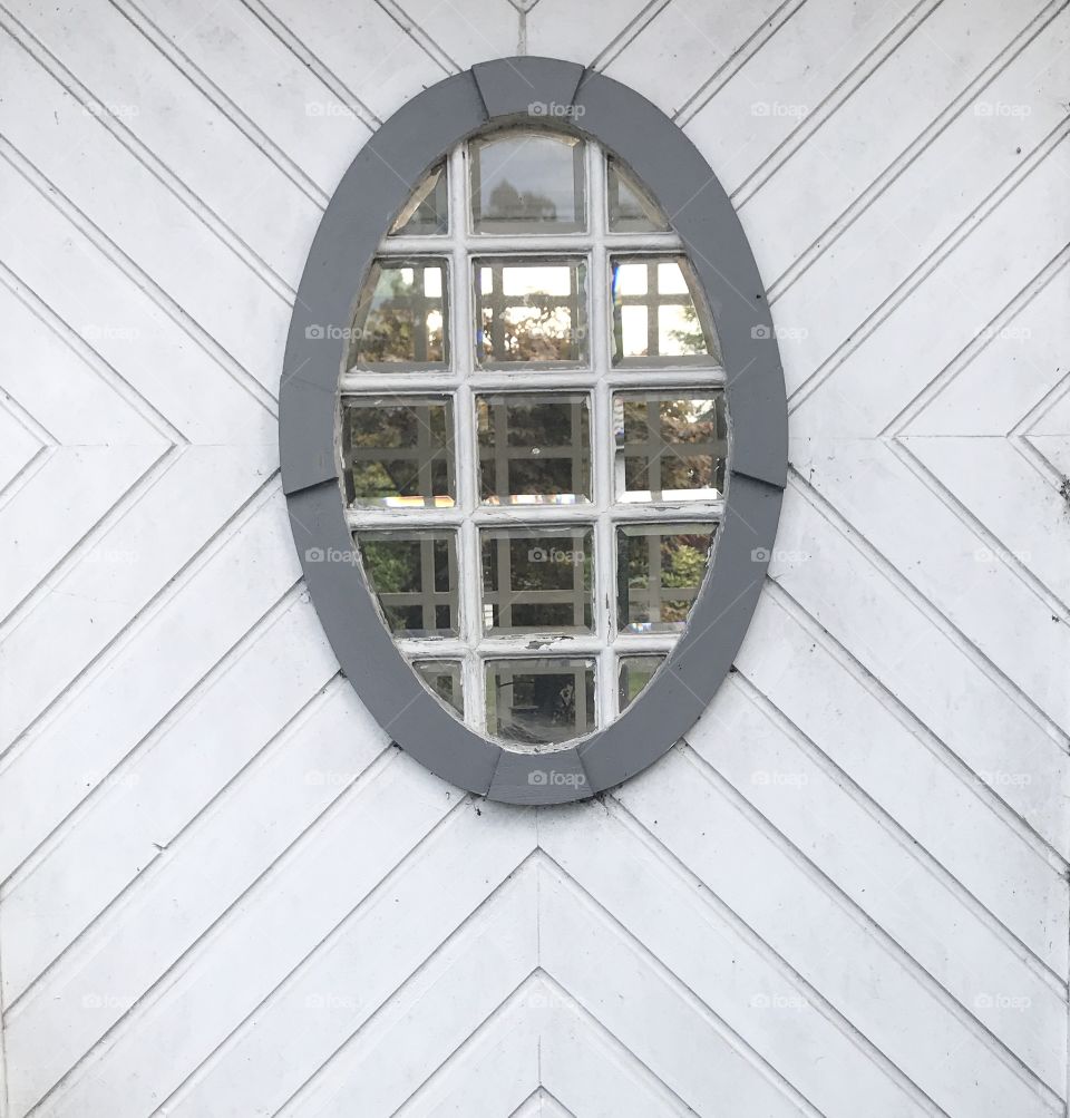 
Front view: Oval window in old gazebo with faceted glass and white wood paneling.