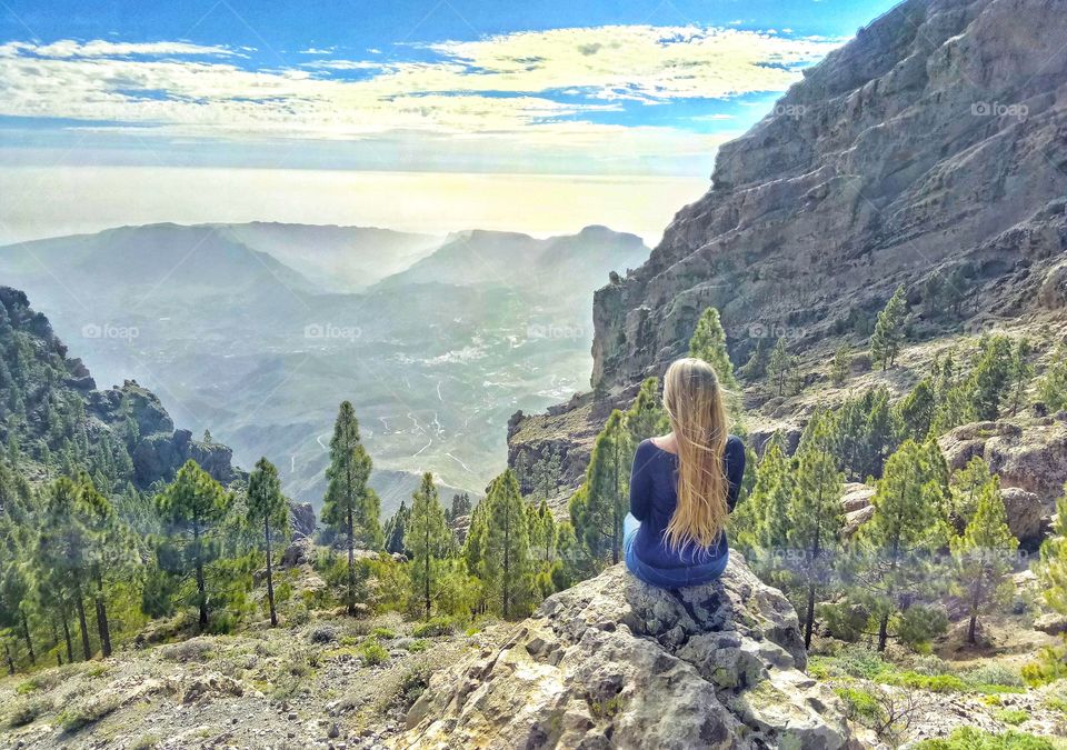 blonde woman sitting on rock in mountains of gran canaria canary island in spain - pine tree forest and valley view