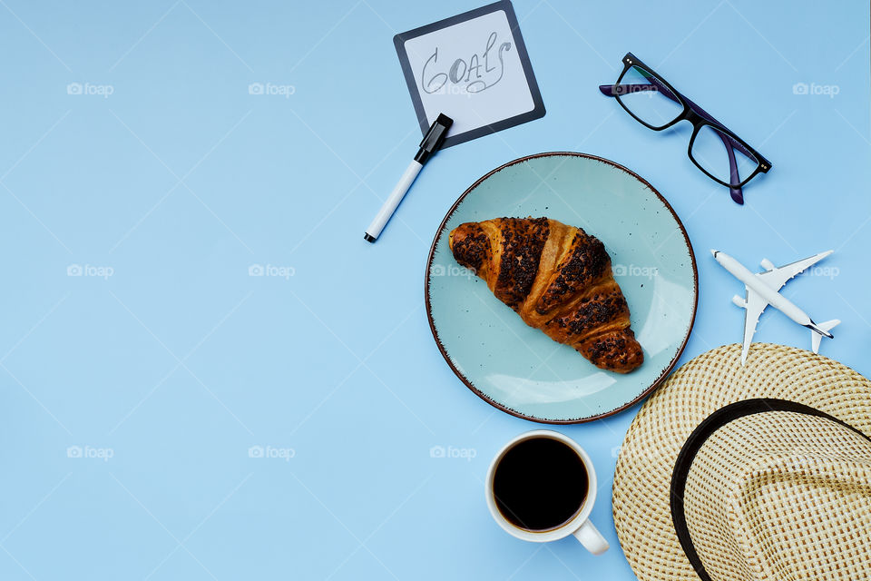 Businessman working morning with cup of hot black coffee, beach hat, croissant, eyeglasses and toy airplane on blue background. Top view, copy space, mockup. flat lay. creative travel, holiday concept.