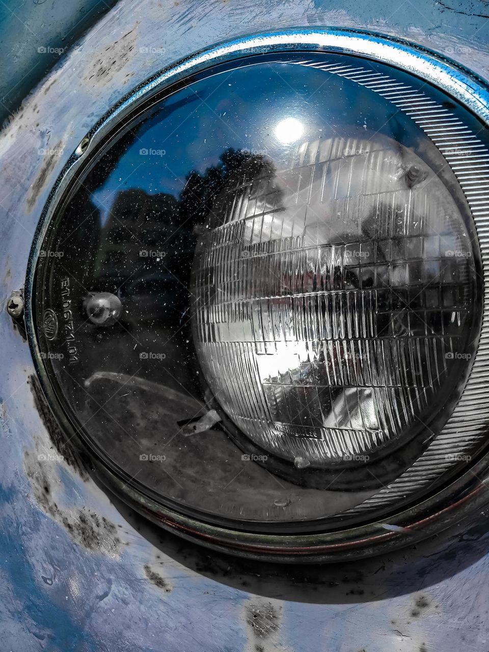 Close up of a headlight from a vintage beat up rustic Volkswagen Bus reflecting the serene view 