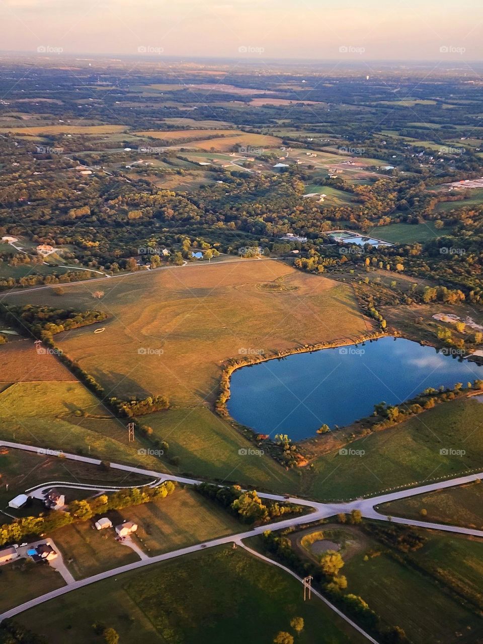 A lake reflects a small puffy cloud as the sun sets creating long shadows over colorful fields