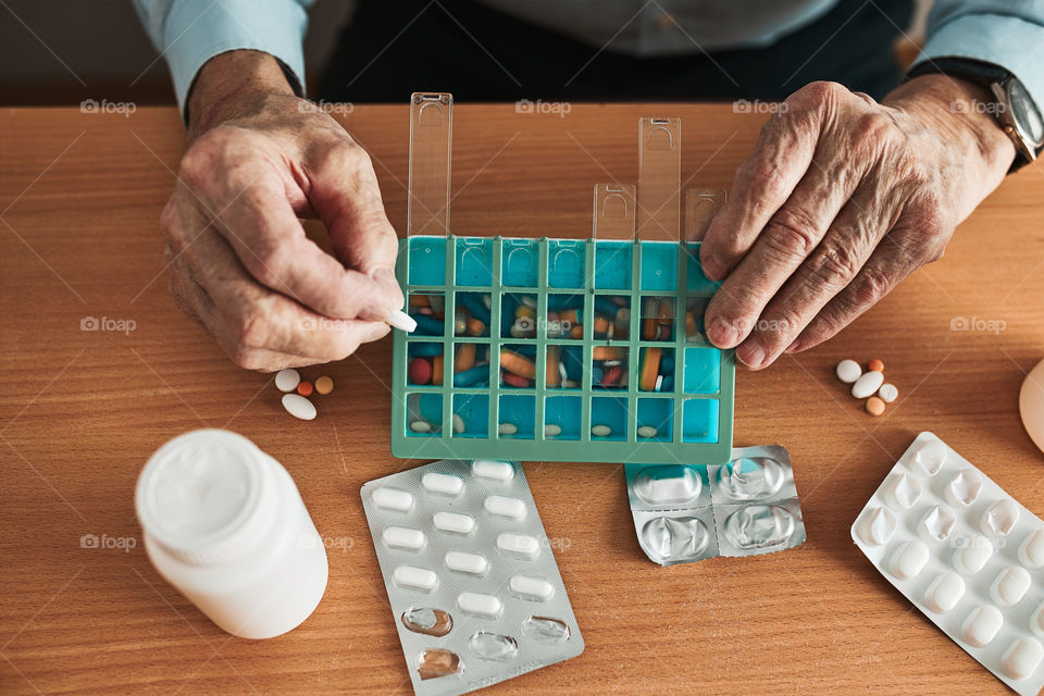 Senior man organizing his medication into pill dispenser. Senior man taking pills from box. Healthcare and old age concept with medicines. Medicaments on table