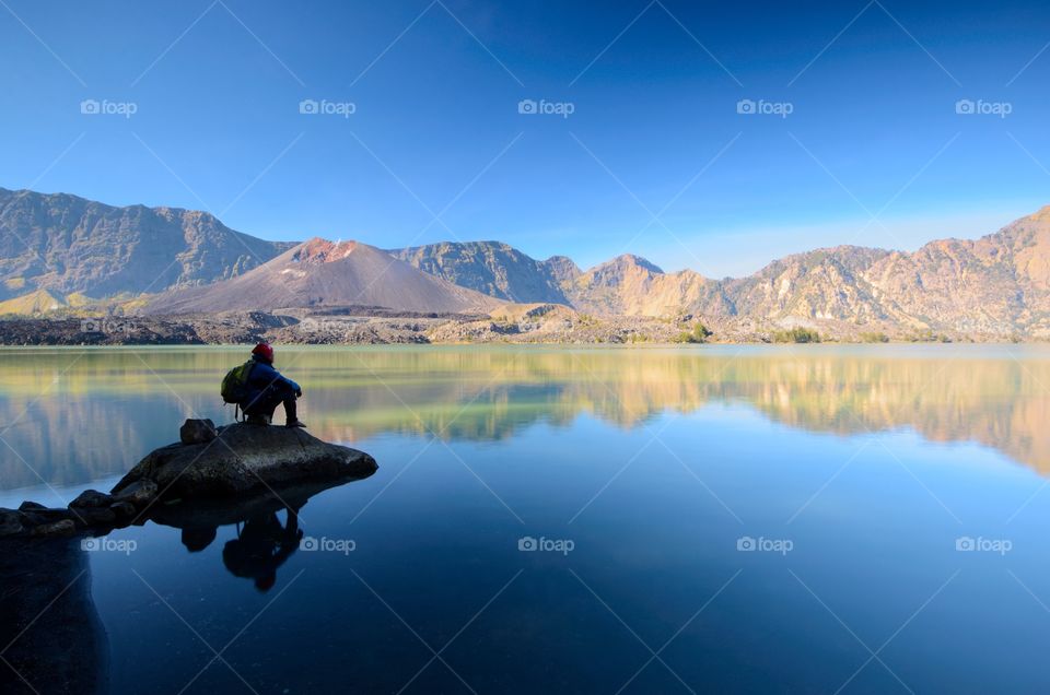 Beautiful nature background with unidentified hiker at Segara Anak Lake in early morning. Mount Rinjani is an active volcano in Lombok, indonesia. Soft focus due to long exposure.