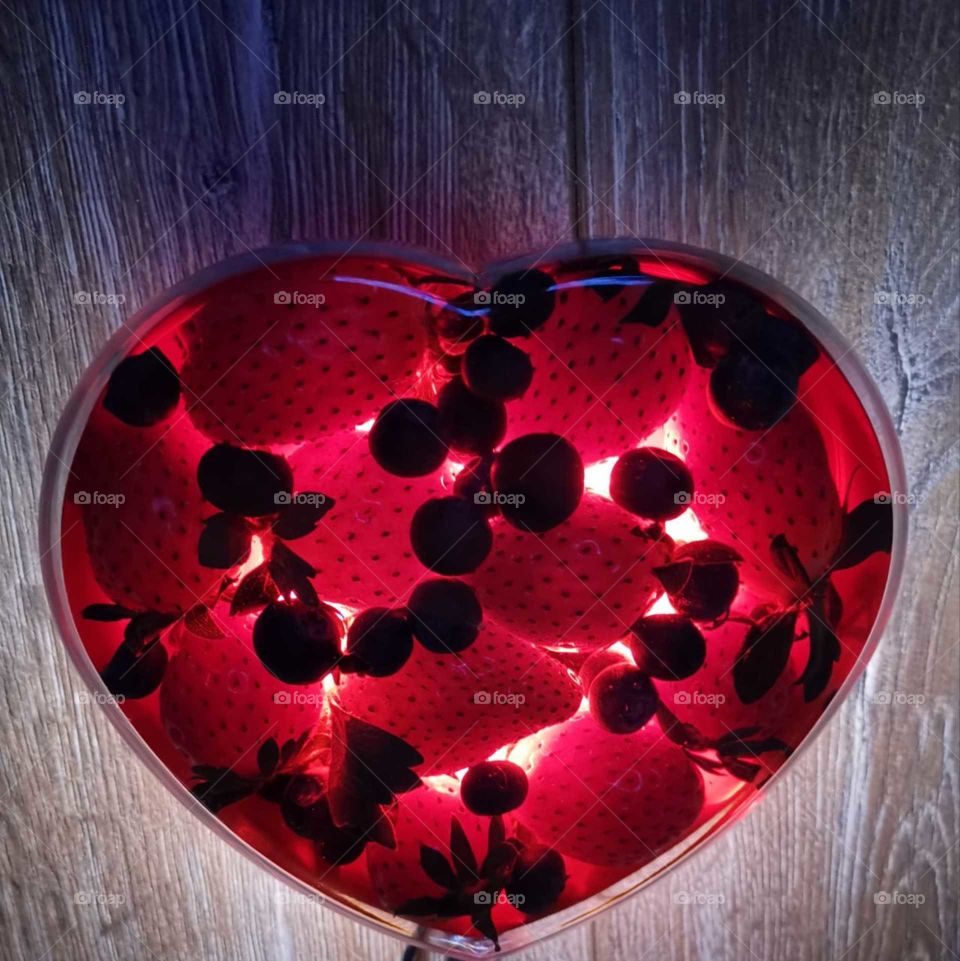 Strawberries and blueberries in a heart-shaped plate with bottom lighting