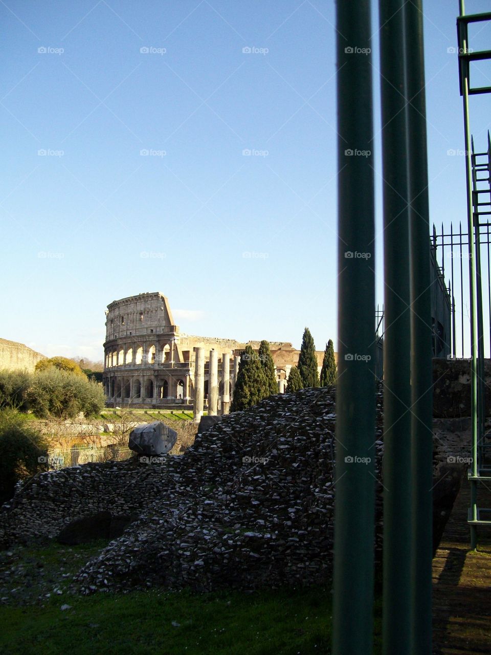 A glimpse of the Roman Coliseum bathed in light juxtaposed with the metal gates in the foreground 