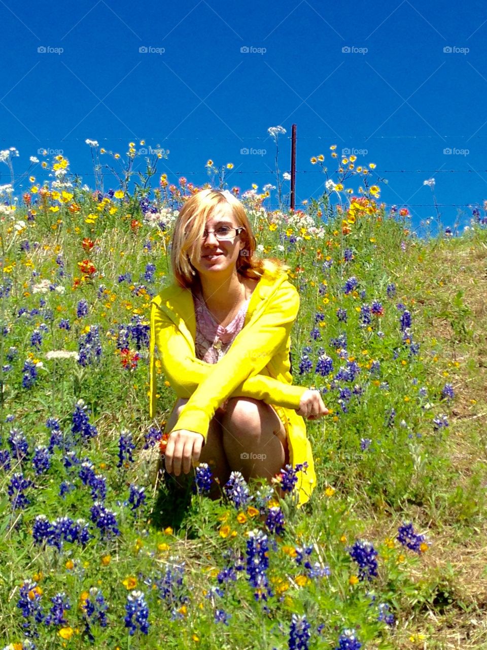 Blonde woman in spectacle sitting on flowers field