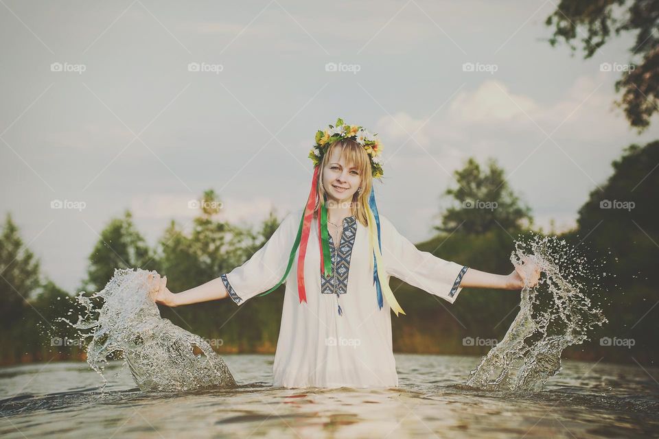 Happy Ukrainian girl,  woman in embroidery, wreath of flowers swimming in green lake in summer. Support Ukraine. Symbol