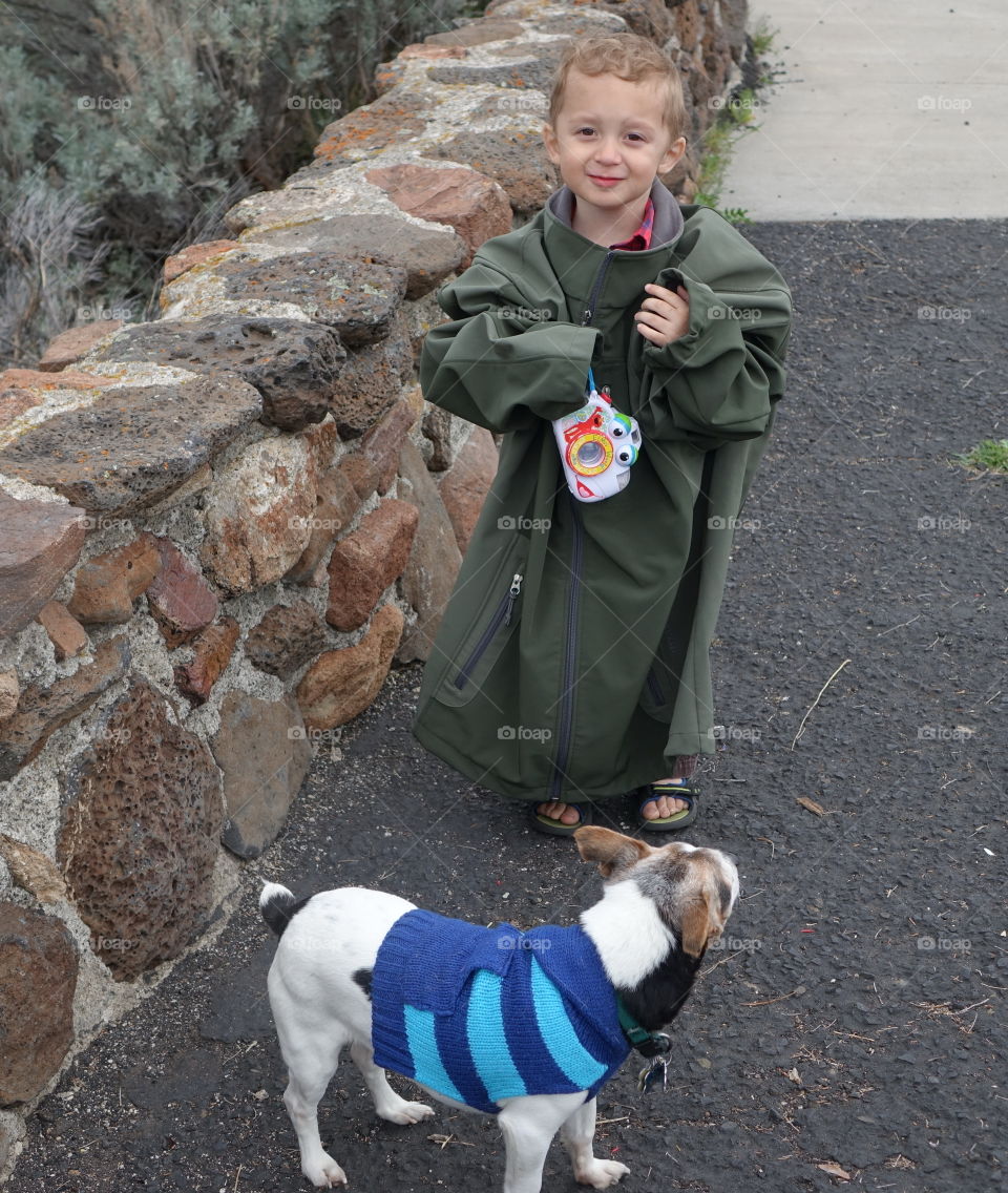 A cute little boy with his toy camera draped in an adult coat with his little Jack Russell Terrier adorned with a sweater in Central Oregon on a chilly spring day. 