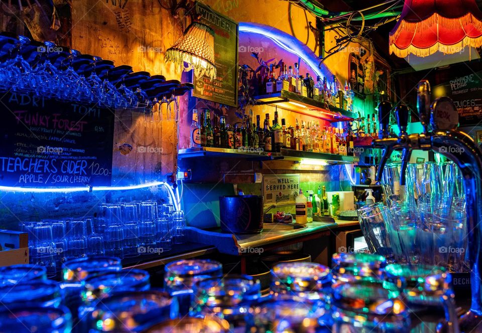 Glasses and bottles of drinks in colorful bar with neon lights
