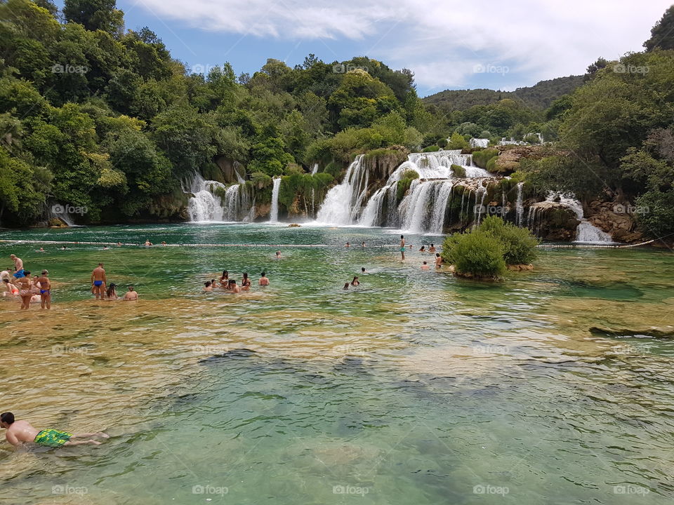 tourists swimming on summer day at kirka waterfalls, in Croatia, colors of blue and green