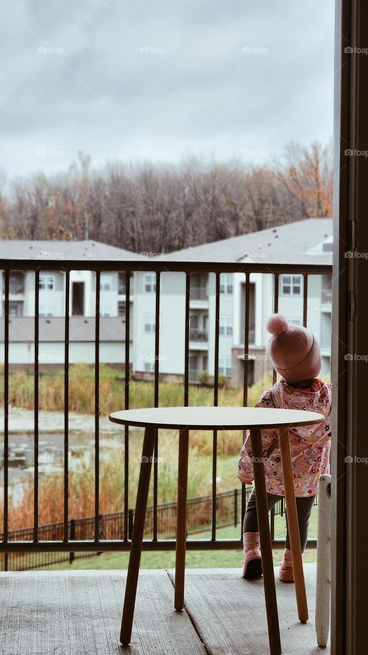 Standing on the balcony, gazing at the serene winter landscape. The cold breeze brushes through as she takes in the beauty of nature, wrapped in the calmness of the season. A perfect blend of innocence and tranquility in this chilly weather