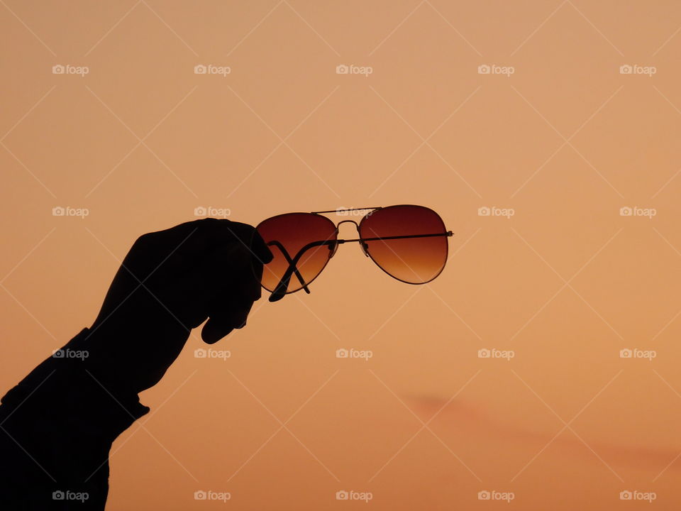 Silhouette image - sunglasses hold in hand with after sunset golden light background. it is creative image.