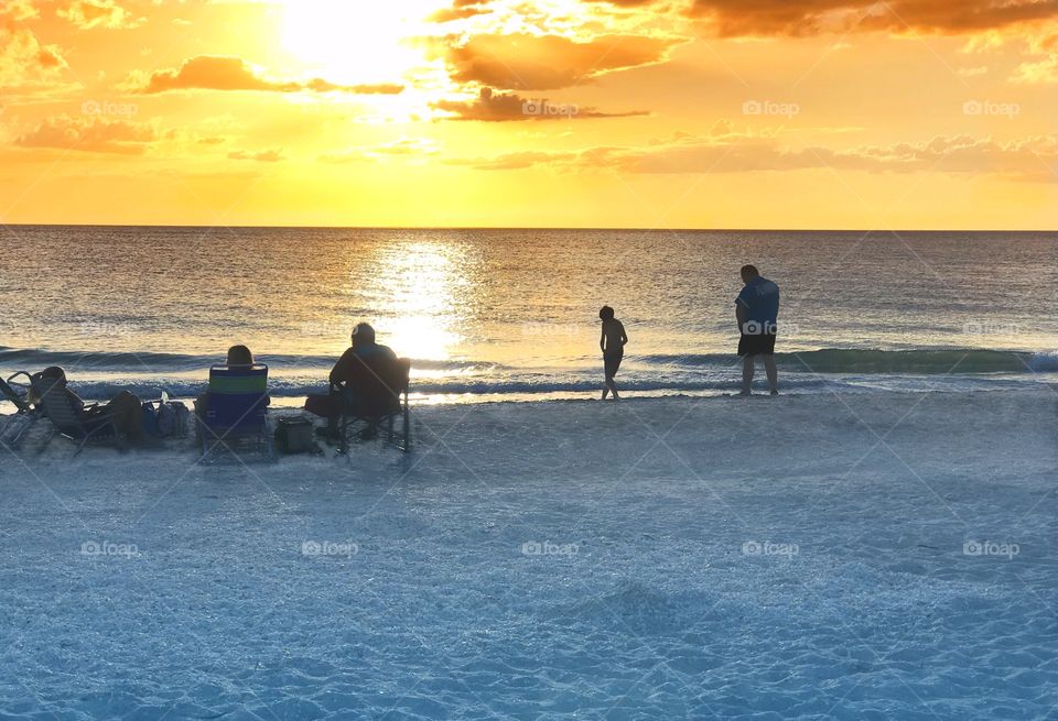 Families on the beach enjoying the calm ocean waves and the dazzling golden sunset.