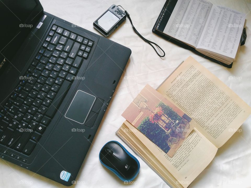 Laptop, book, notebook, computer mouse and camera are on the table