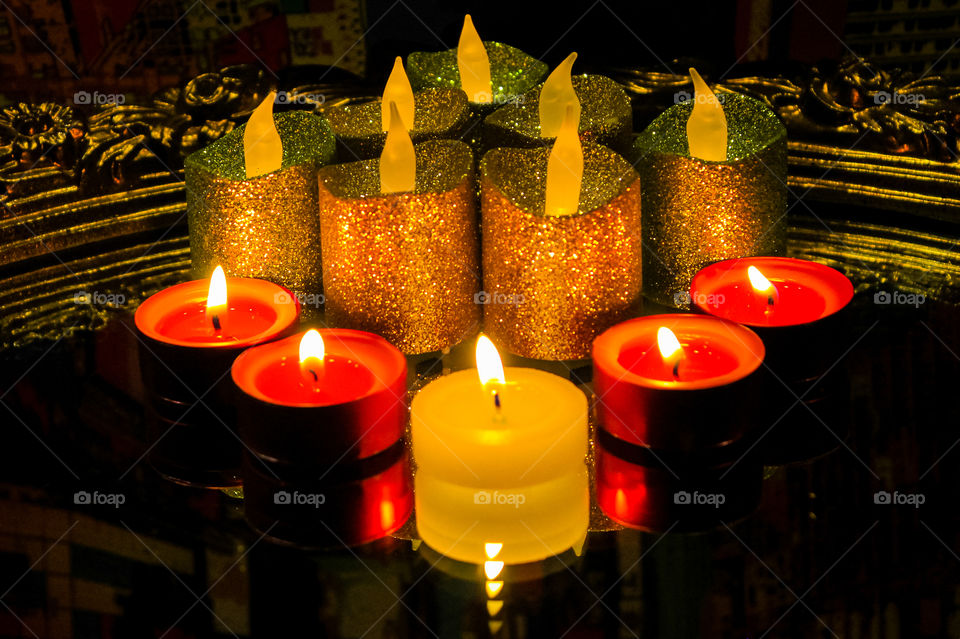 Night: Wax and battery powered candles are alit on a mirror with an ornate gilded frame. Images of the candles and the flames are reflected in the mirror along with reflection of a painting used as colourful backdrop behind the mirror. 