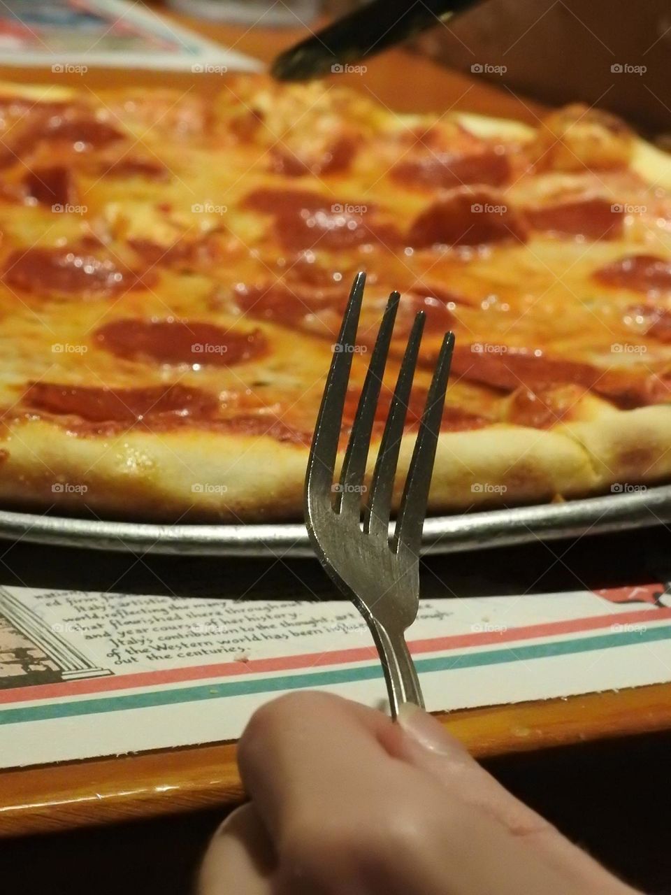 Teen holding a fork getting ready to eat his warm just ready pizza at an Italian restaurant.