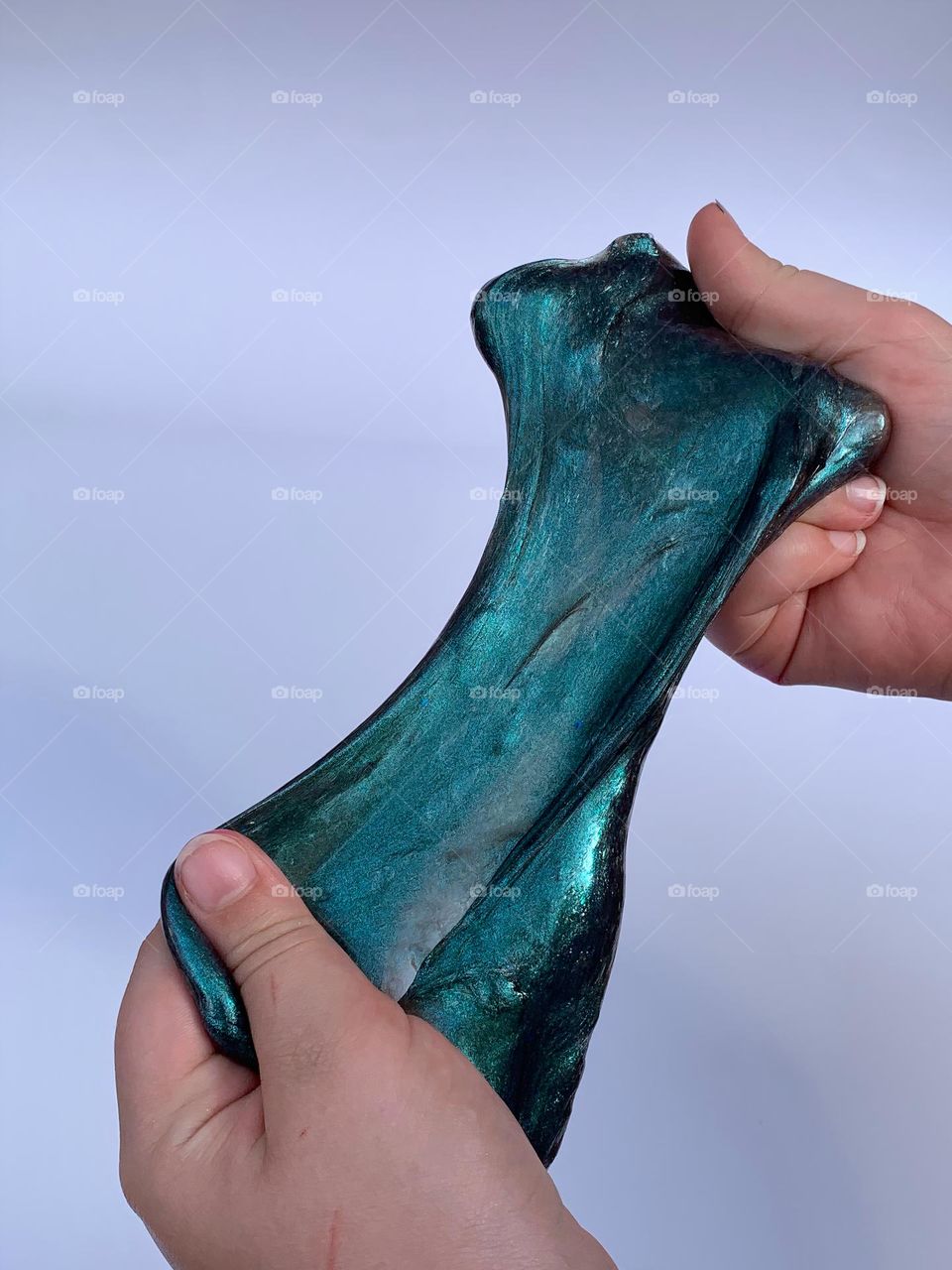 Turquoise Teal Metallic Color Slime Stretched And Held By A Child’s Two Hands With A White Background.