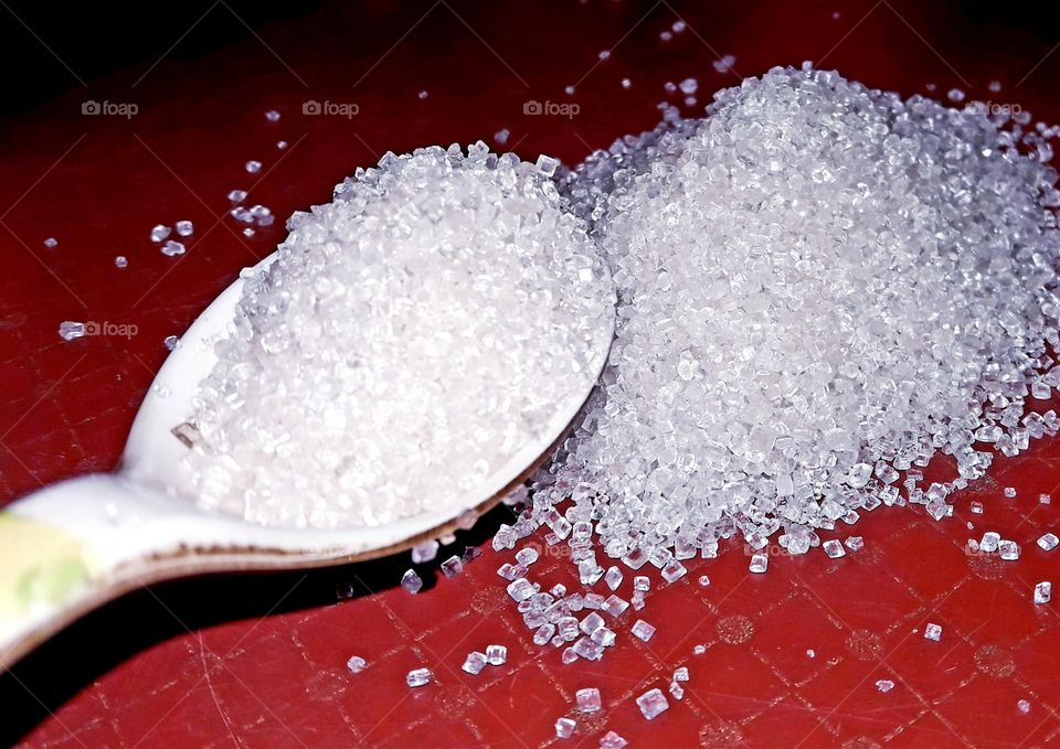 White colour sugar on red colour table and a tea spoon
