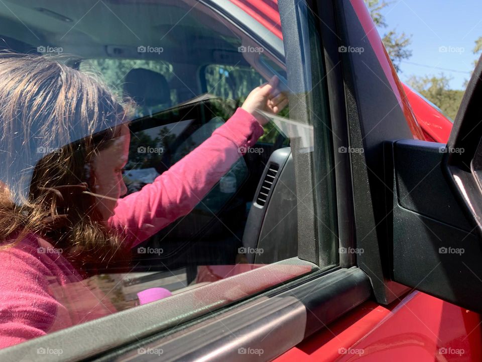 Commuting: child dresses in pink and purple climbing in the high pickup truck to go somewhere holding the passenger seat handle to help to sit in the vehicle, seen through the passenger side window.